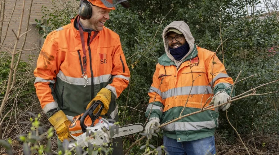 twee mannen staan in een perkje waarbij een man snoeit